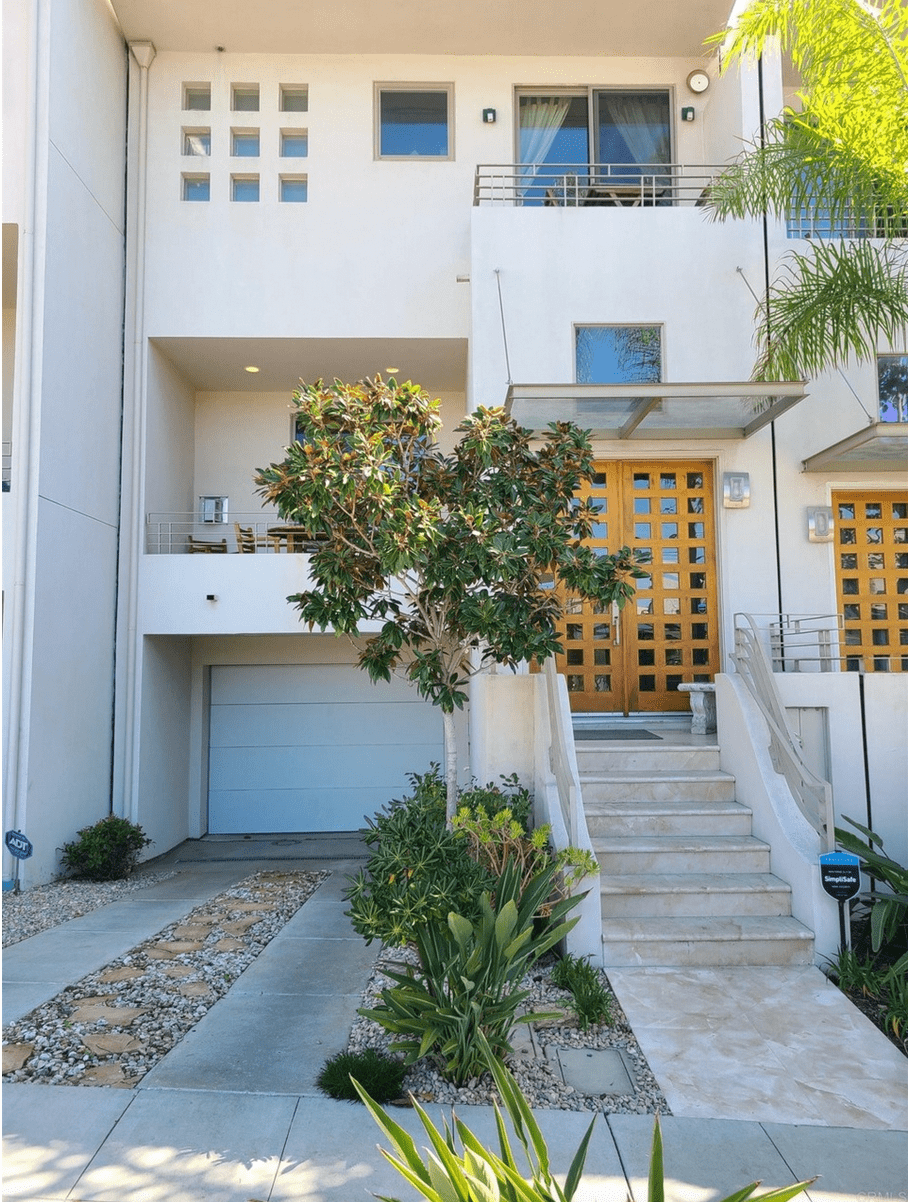 The exterior of a cream stucco condo with a balcony and trees outside